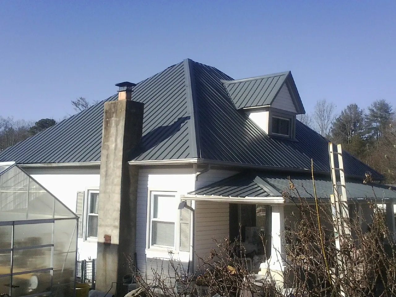 Dark blue standing seam metal roof on a white farmhouse with dormer — Slate & Tile Roof Repair by Roofing Brothers in Sanford