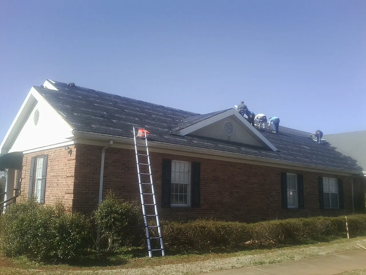 Crew tearing shingles off a brick ranch roof with a ladder set — Metal Roof Repair work by our crew in Sanford