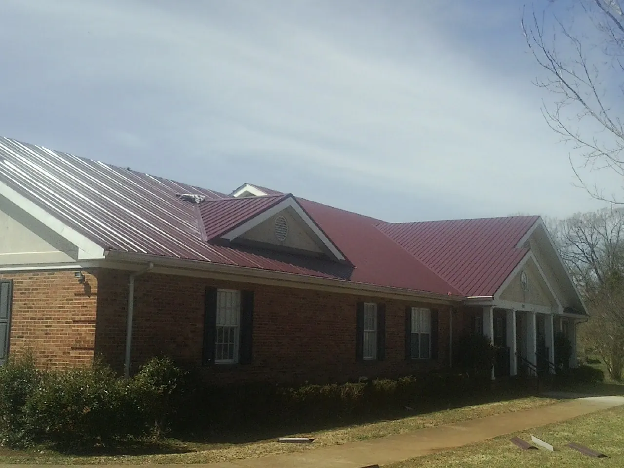 Red metal roof with gabled entries on a long brick building, from a Hail Damage Roof Repair job in Sanford