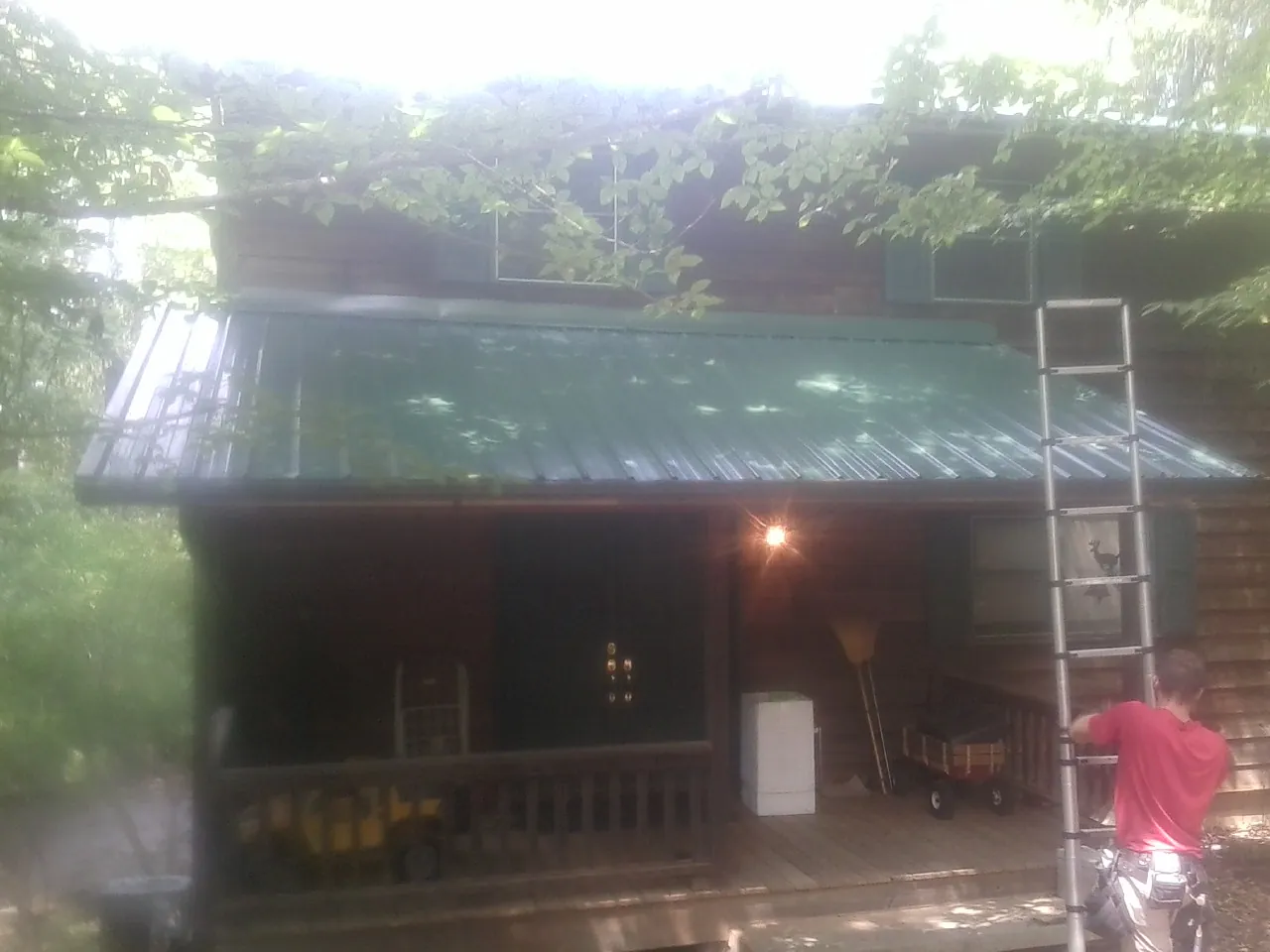 Worker on a ladder at the green porch roof of a wooded cabin in Sanford