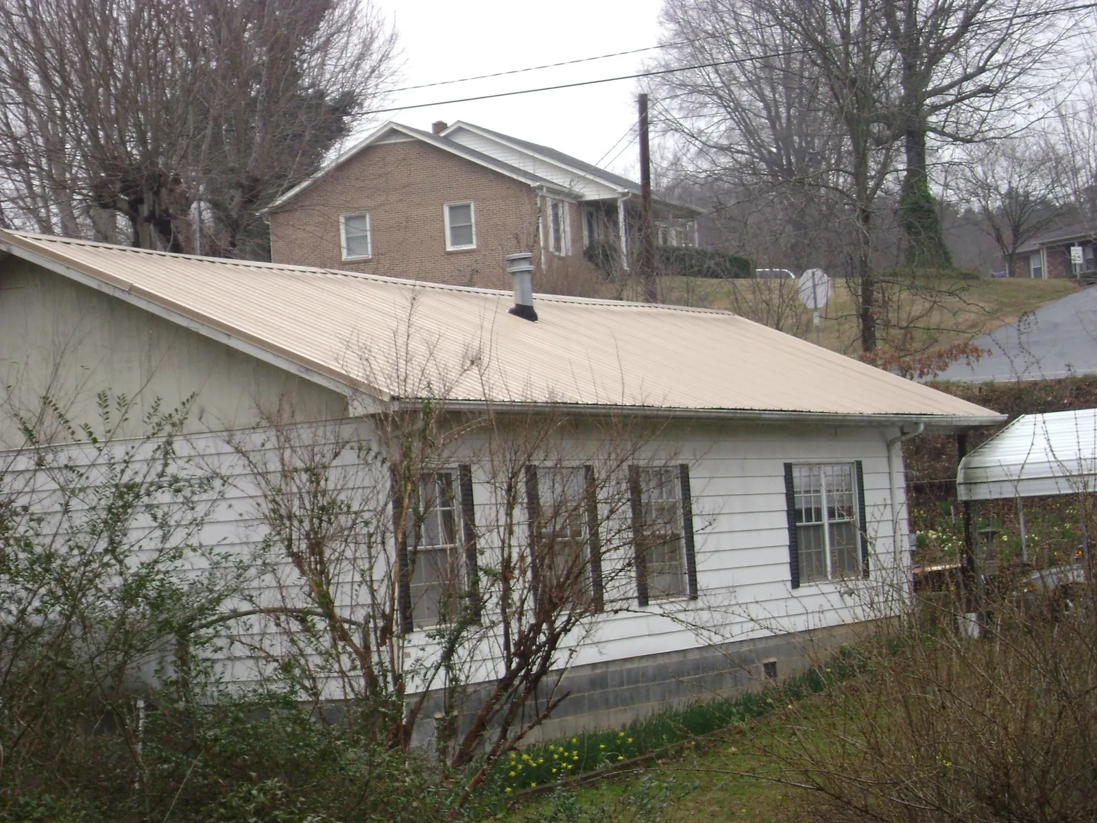 Tan metal roof on a white sided house set into a hillside — Commercial Roofing by Roofing Brothers in Sanford